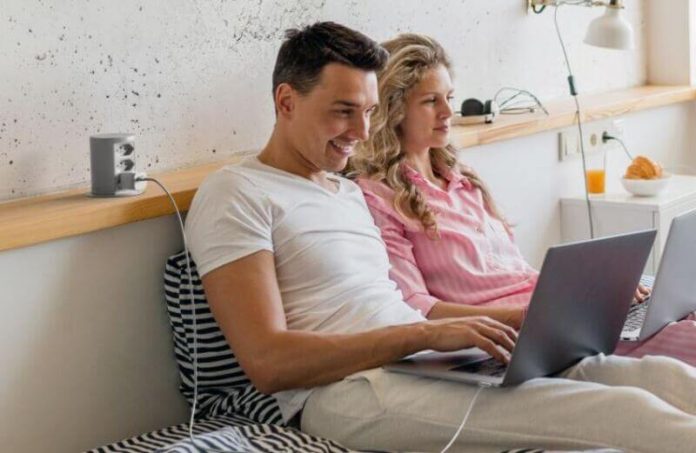 Tomada para móvel instalada na cabeceira de uma cama, onde um casal usa um notebook.