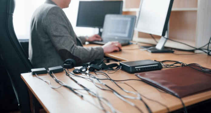 Mesa de escritório com vários fios e cabos desorganizados sobre ela.